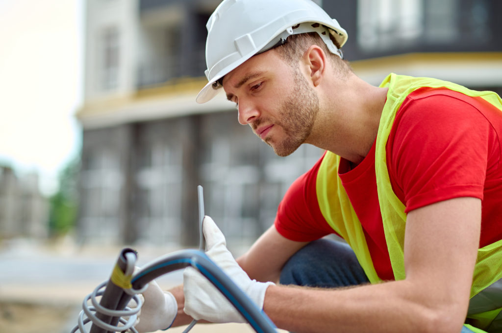 adjustment-young-adult-man-protective-helmet-gloves-bright-vest-crouching-looking-tool-sideways-camera-construction-site.jpg